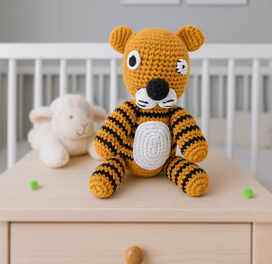 Handmade crochet tiger stuffed animal in mustard white with black stripes displayed in nursery with white cribs and children's wall art
