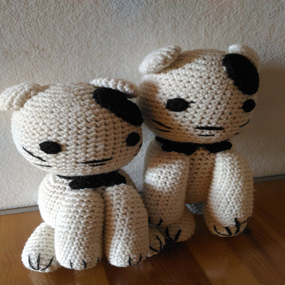 Two handmade crochet amigurumi cats sitting side-by-side on a wooden surface.