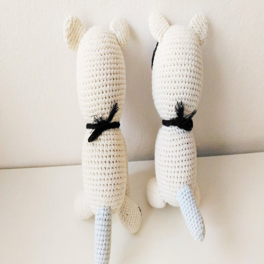 Back view of a pair of handmade amigurumi crochet cats with long tails sitting together