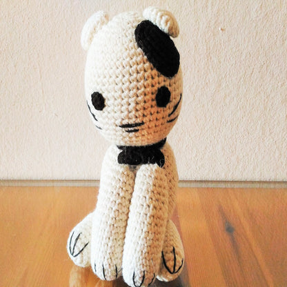 Close-up of a small, handcrafted yarn kitten sitting on a polished wooden tabletop, highlighting the intricate crochet stitches and soft texture