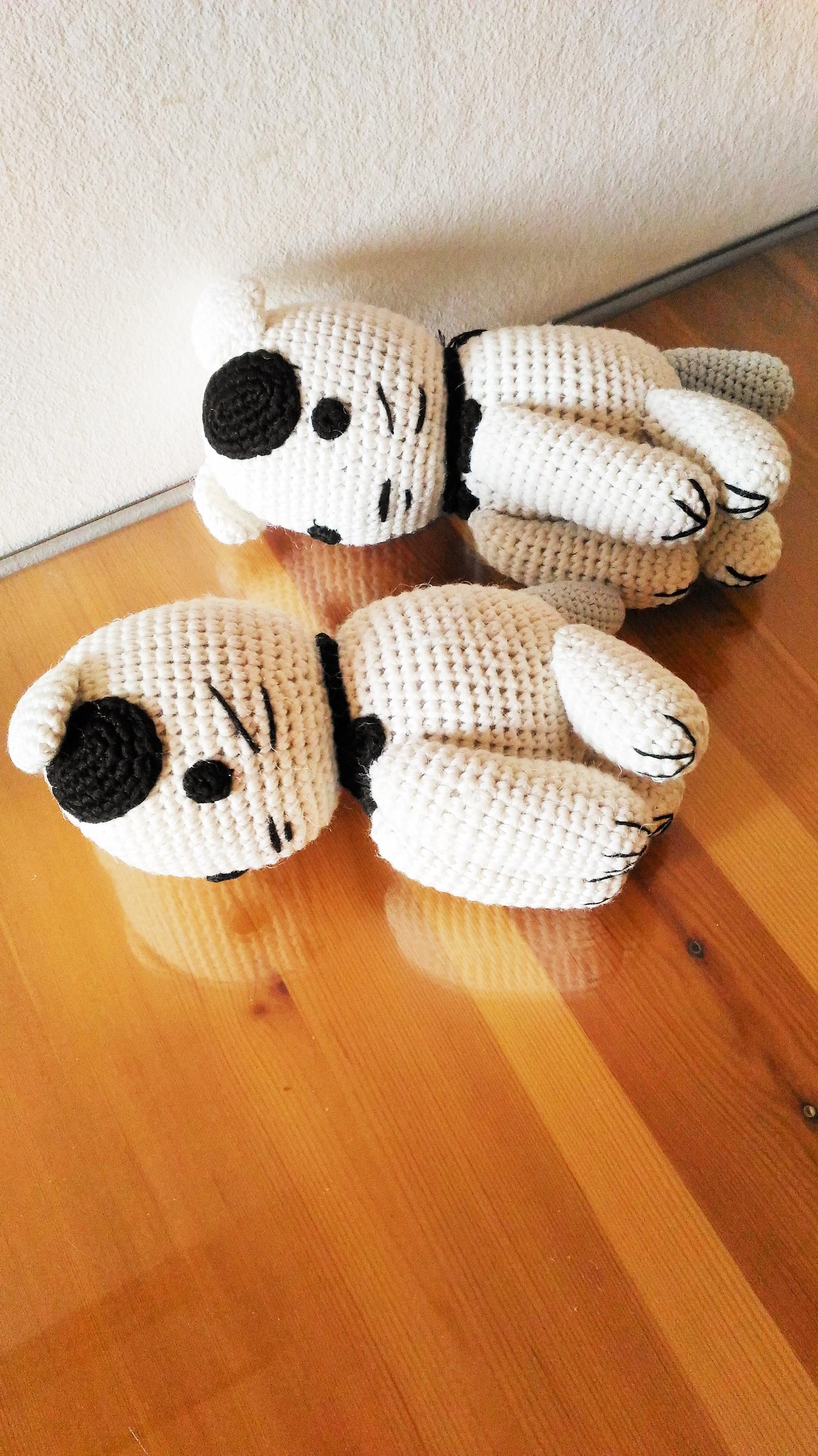 Two handmade amigurumi cats sleeping on a rustic wooden glass table surface