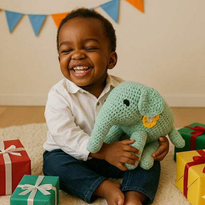 A smiling child holding a green handmade crochet elephant surrounded by colorful gifts