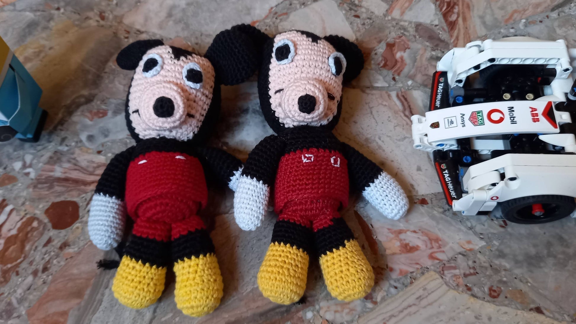 A lifestyle view of two handmade mouse amigurumi toys in a nursery, shown next to building blocks and a toy car; highlighting part of a cozy child's play area