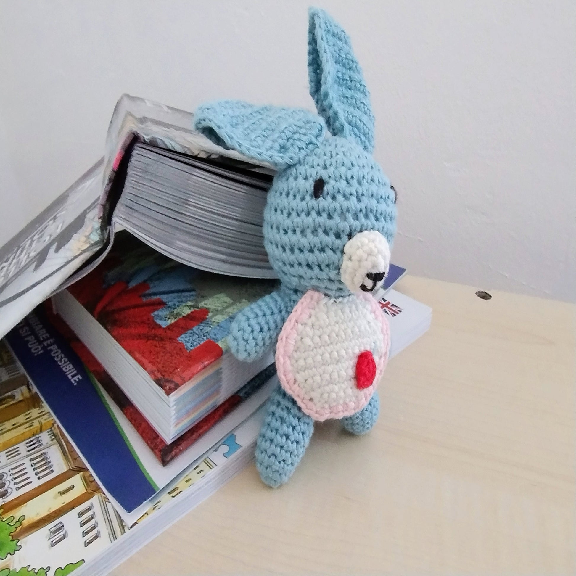 Handmade koala amigurumi sitting on a wooden table next to books, used as a decorative accent piece for a study or nursery