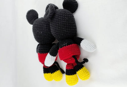 Set of back view of a handmade mouse amigurumi laying down, featuring iconic red shorts and yellow shoes with a detailed crochet tail; an artisanal nursery toy